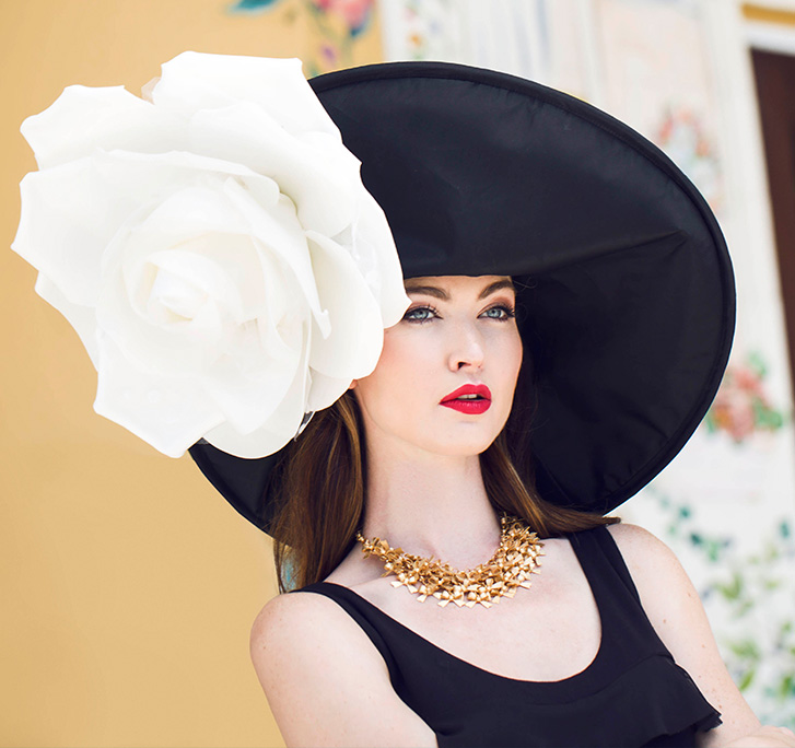 A woman wearing a black dress and large, ornate hat.